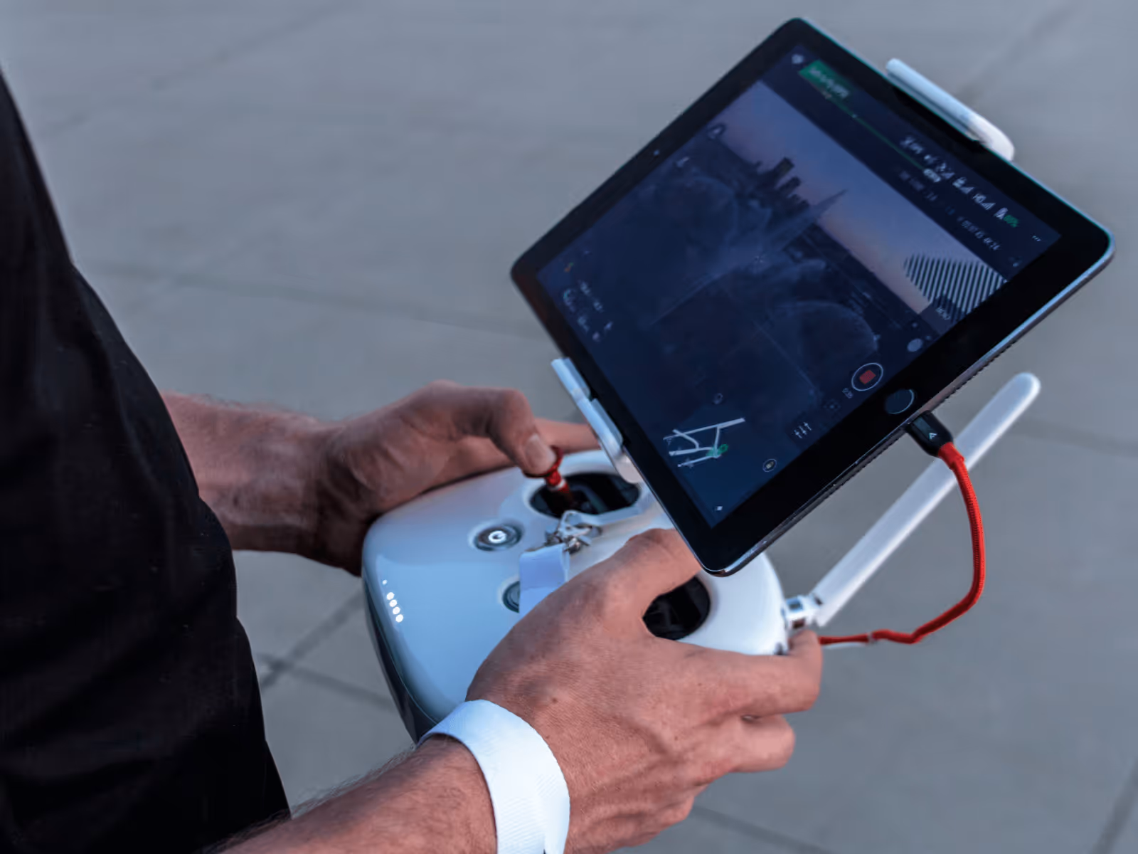 Person holding a drone remote controller with a tablet attached displaying a live aerial view.
