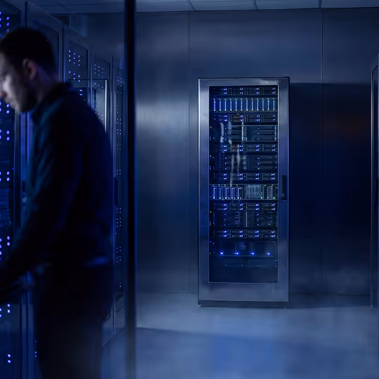 Homem trabalhando em um data center com servidores iluminados em um ambiente escuro e moderno.