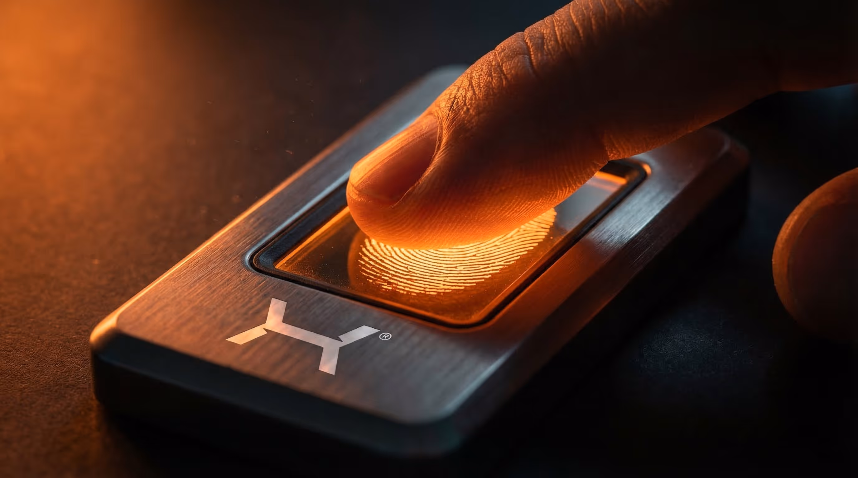 Dedo pressionando um leitor de impressão digital iluminado em luz laranja.