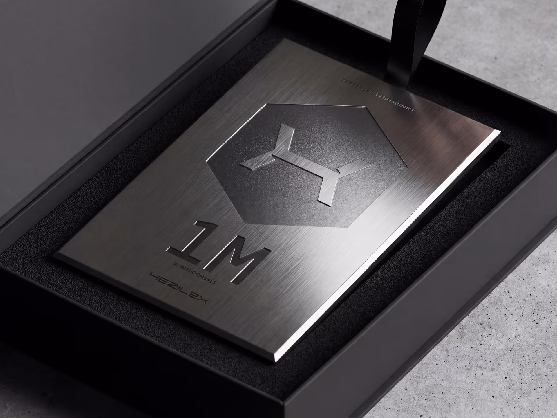 Placa metálica em tom cinza escuro com o símbolo Hezilex, indicando 1 milhão em retiradas, apresentada em uma caixa preta com interior macio.