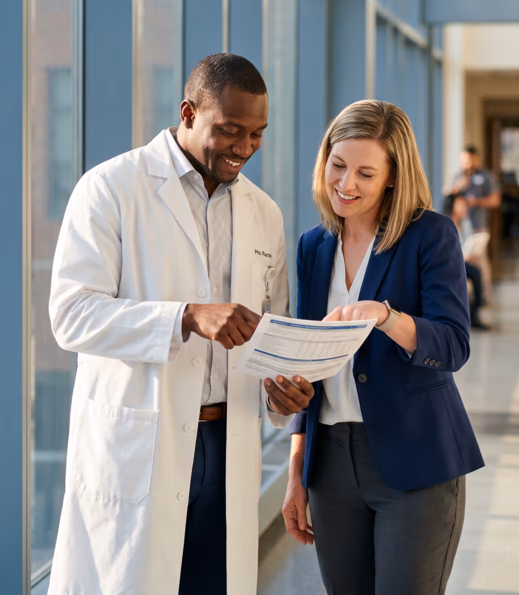 Doctor and businesswoman smiling while reviewing a document together in a bright hallway.