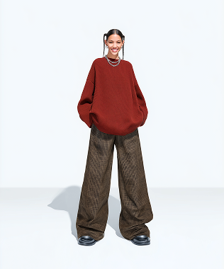 Smiling woman wearing an oversized rust-colored sweater and wide-leg brown pants with black shoes against a white background.