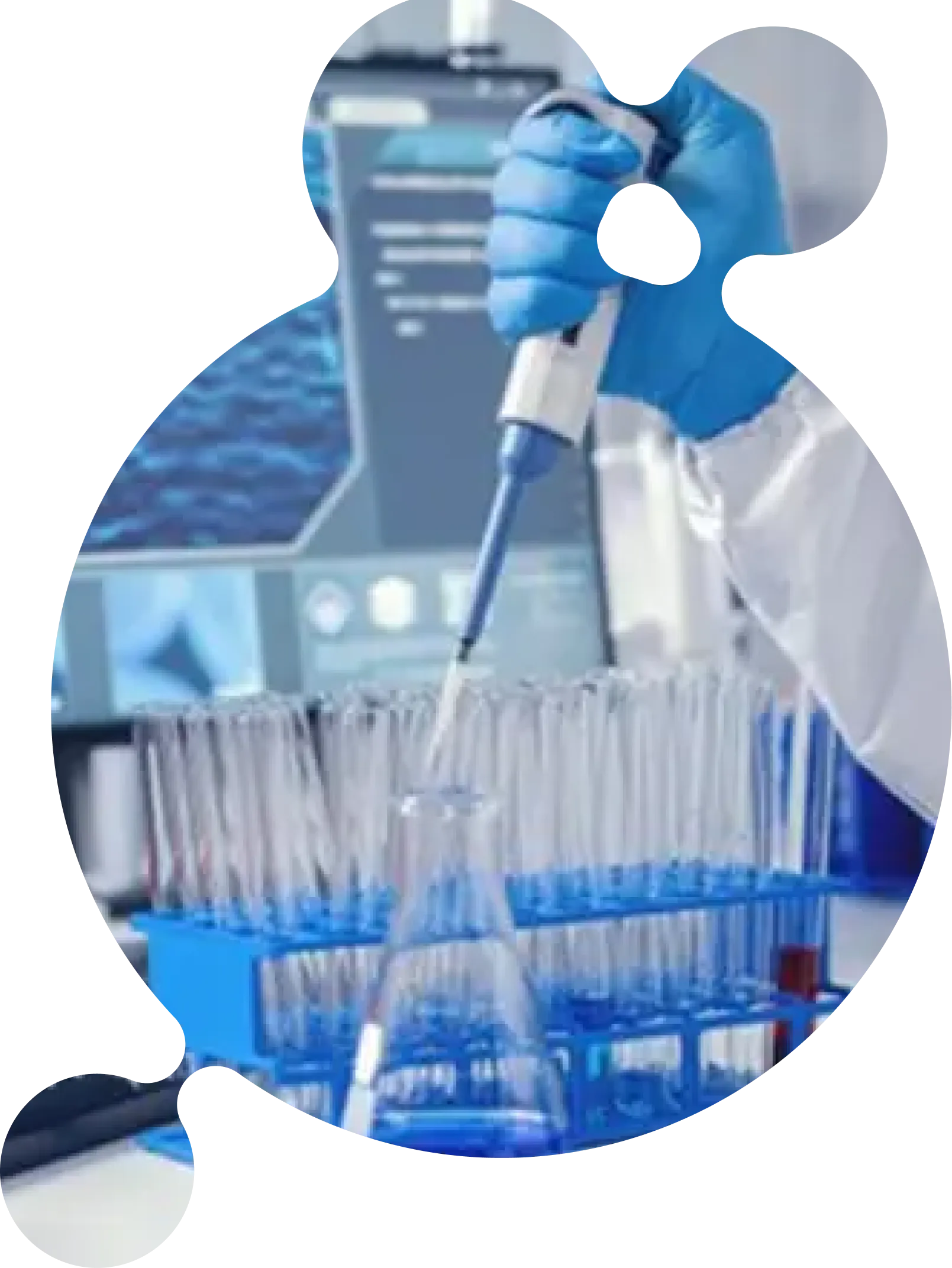 A laboratory researcher in blue gloves and a white coat using a pipette to transfer liquid into test tubes arranged in a rack, with lab equipment and a monitor visible in the background.