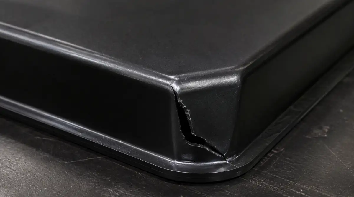 Close-up of torn plastic corner on a deep-draw vacuum formed part showing over-softening failure
