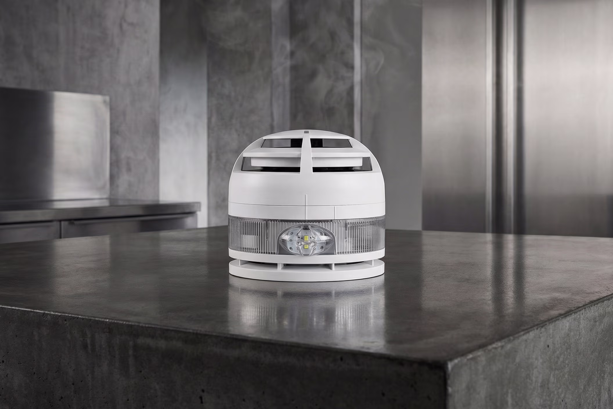Rookmelderapparaat met LED-lampje op beton in een industriële omgeving.