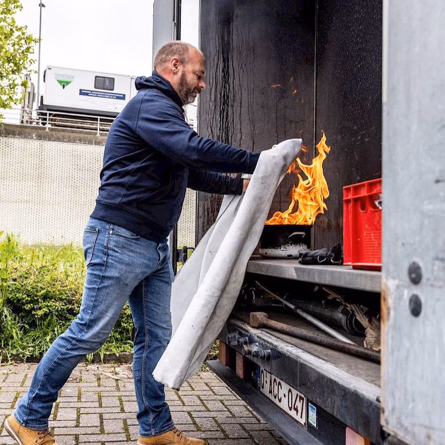 Un homme éteint le feu à l'aide d'une couverture anti-feu dans le hayon d'un camion en feu.