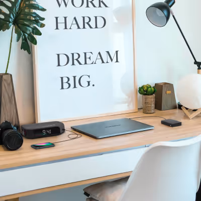 Espace de travail moderne avec bureau en bois, ordinateur portable, lampe de bureau, plantes et cadre mural affichant le texte "Travaille dur, rêve grand."