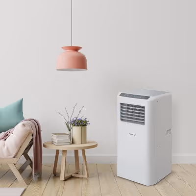 Climatiseur mobile blanc dans un salon minimaliste avec une table ronde en bois, des livres, des fleurs, une chaise avec coussin turquoise et couverture rose, et une suspension rose.