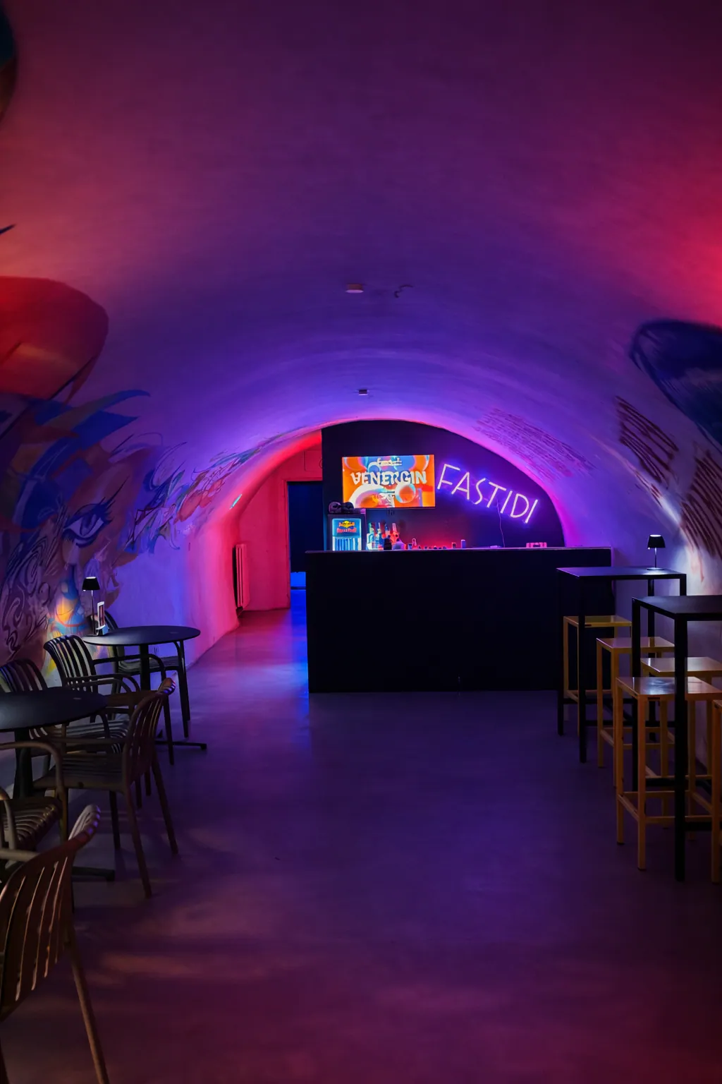 Bar illuminato al neon all’interno di un tunnel ad arco con murales colorati e posti a sedere su entrambi i lati.