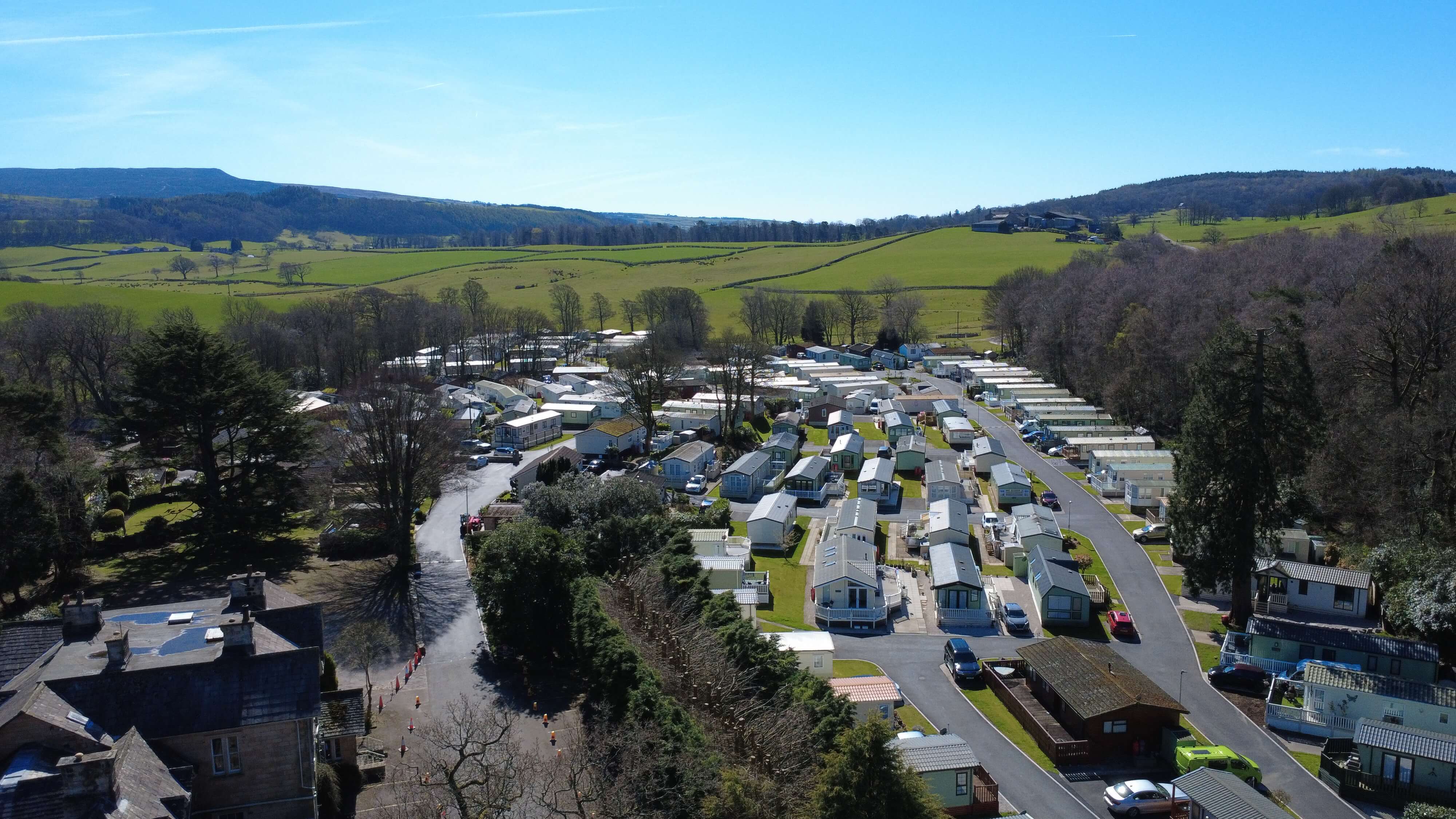 Aerial view of caravan park nestled in green valley surrounded by rolling hills and trees.