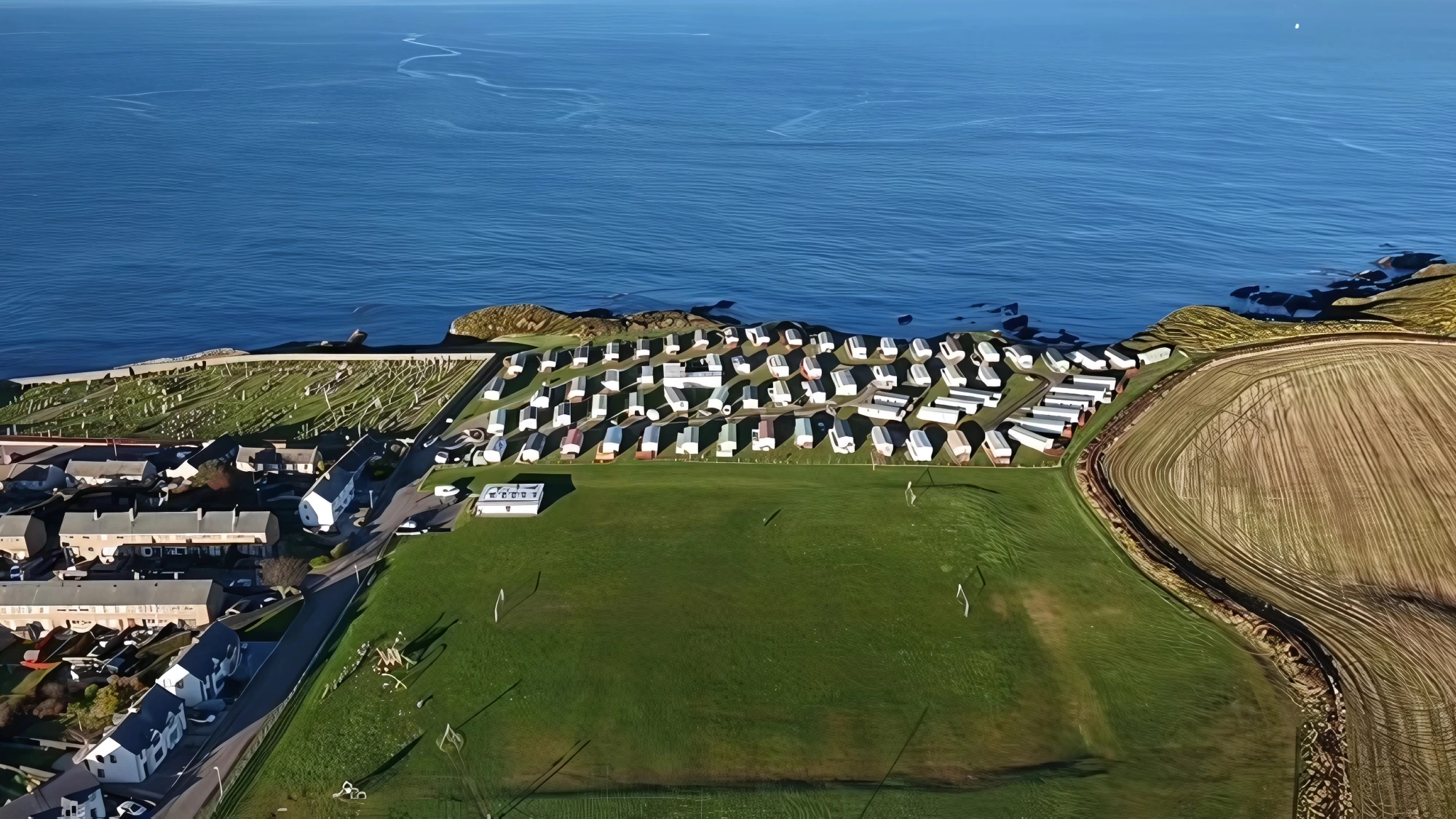 Aerial view of seaside caravan park with white mobile homes on grassy hillside overlooking blue ocean