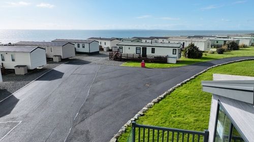 Coastal caravan park with white mobile homes, green grass, and sea view in background