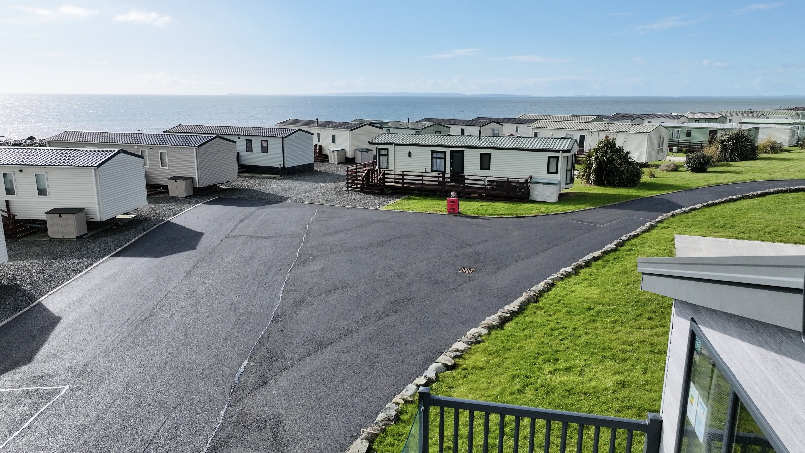 Coastal caravan park with white mobile homes, green grass, and sea view in background