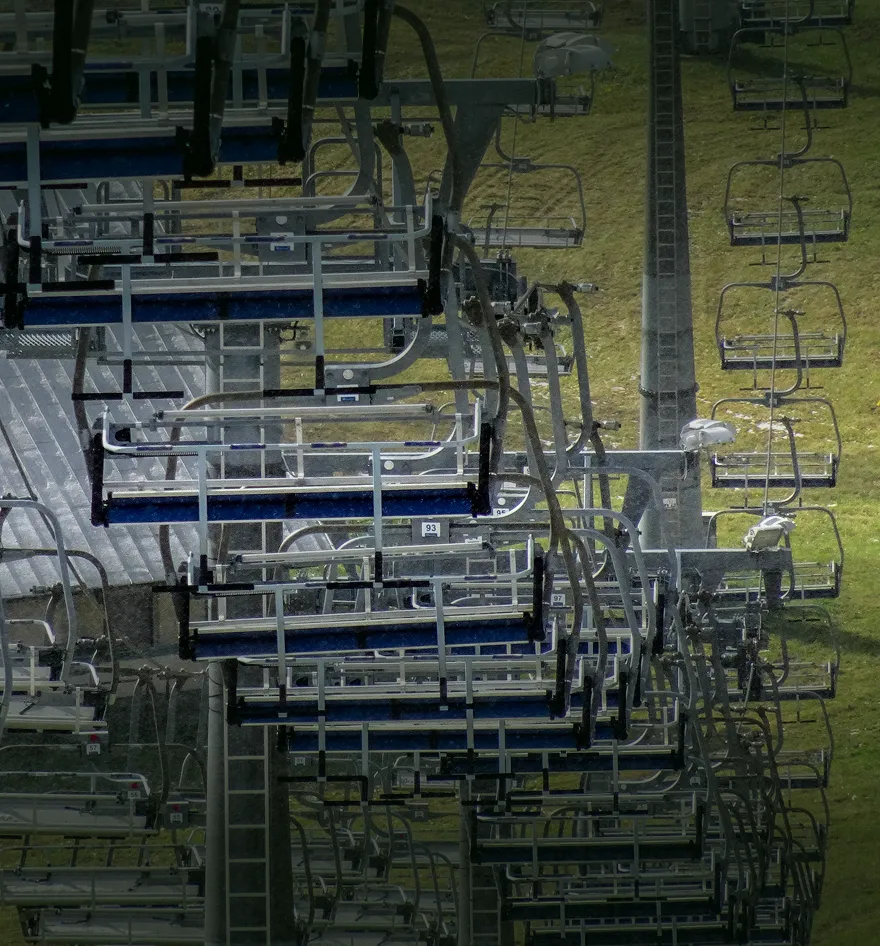 Empty ski lift chairs suspended above grassy terrain on a clear day.