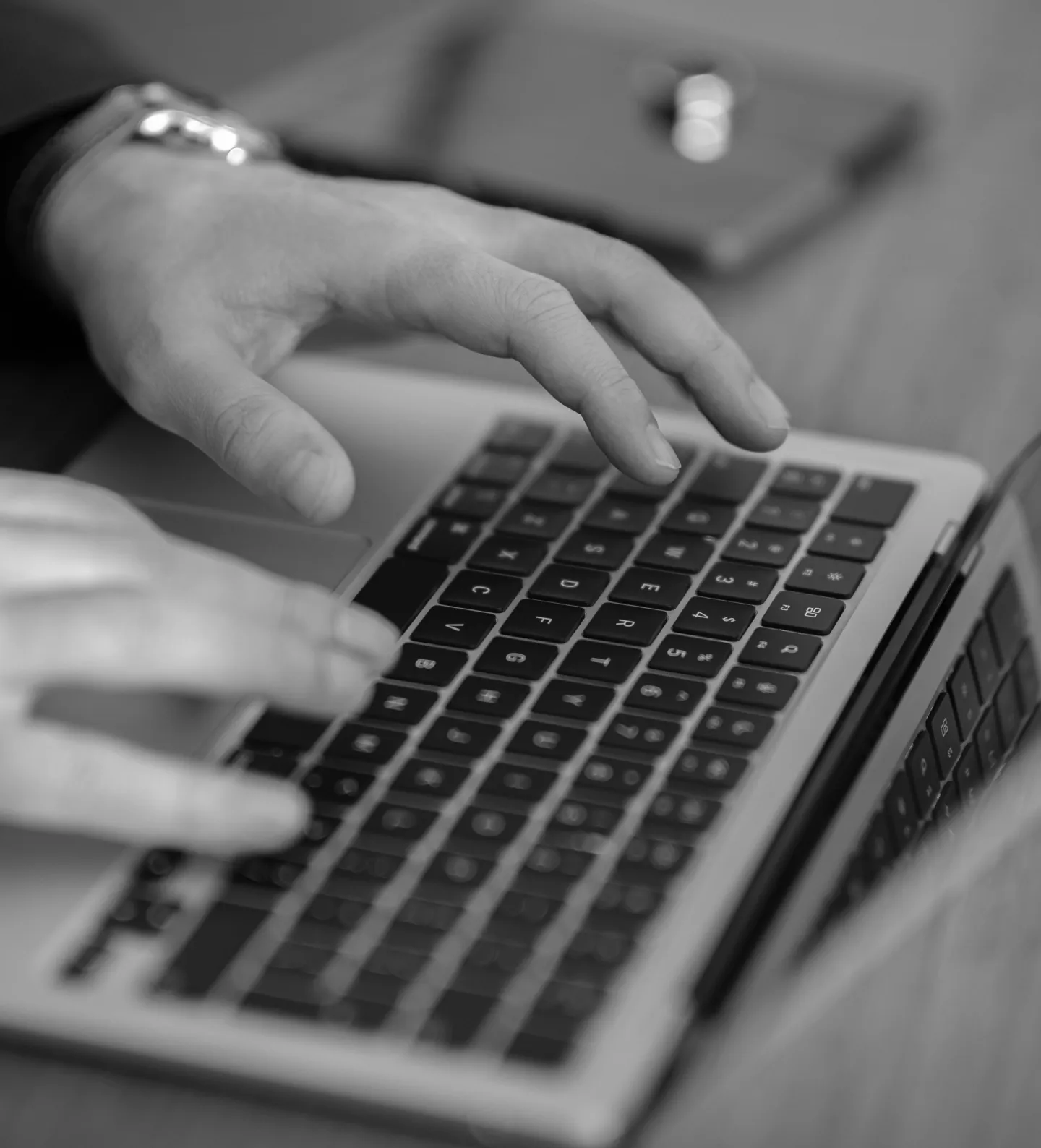 Close-up of hands typing on a laptop keyboard with a blurred object in the background.