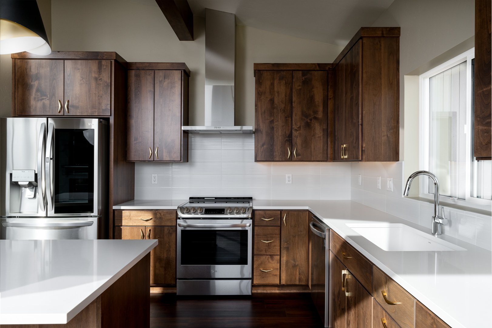 Modern kitchen with dark wooden cabinets, white countertops, stainless steel appliances, and a large window above the sink.