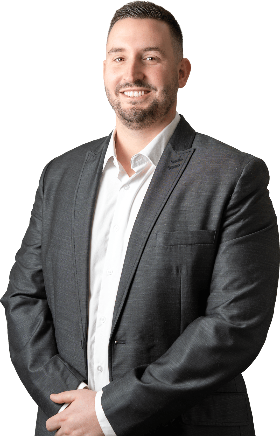Smiling man with short dark hair and beard wearing a dark suit jacket over a white shirt, standing with hands clasped.