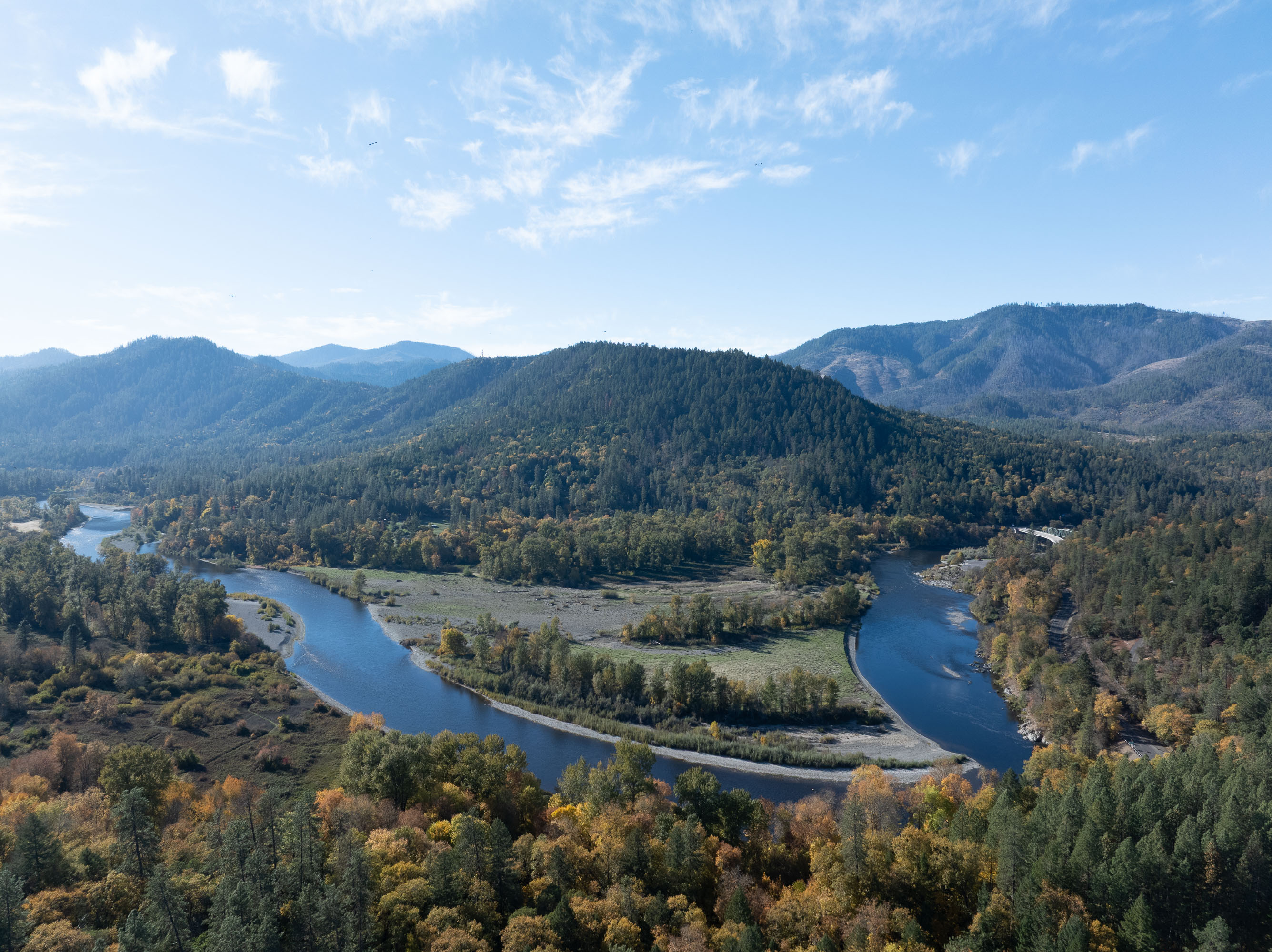 A winding river flowing through a forested mountainous landscape under a blue sky with scattered clouds.