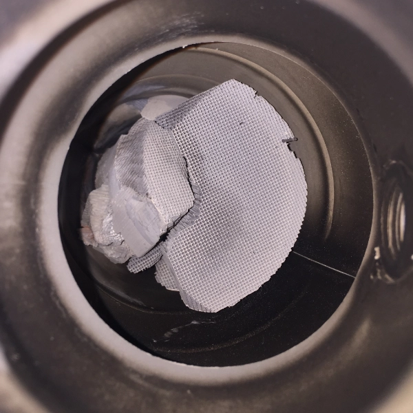 Close-up of a damaged honeycomb ceramic catalytic converter substrate inside a cylindrical housing.