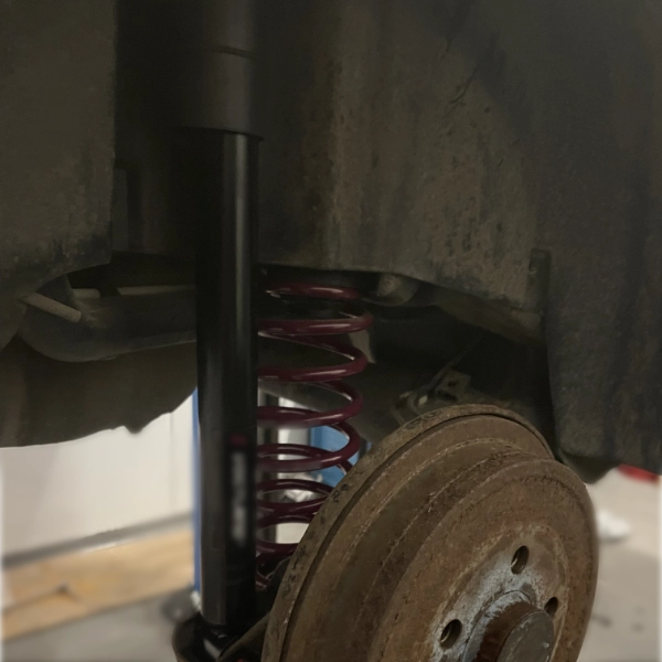 Close-up of a car suspension showing a red coil spring and black shock absorber next to a rusty brake disc.