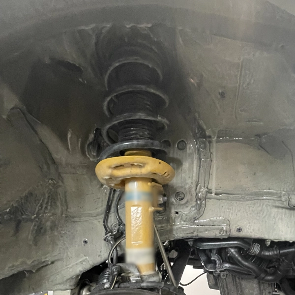 Close-up view of a yellow vehicle suspension strut and coil spring inside a car wheel well.