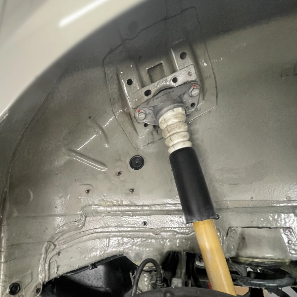 Close-up of a car's rear suspension area showing a shock absorber mounted to the body with bolts and a protective rubber boot.