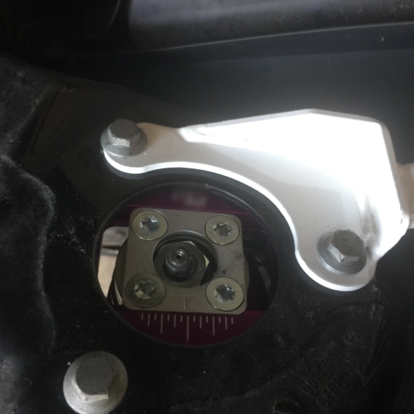 Close-up of a car suspension top mount with visible bolts and adjustment markings inside the strut tower.