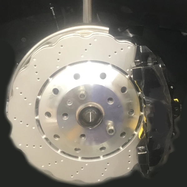 Close-up of a drilled and slotted silver brake disc with a black brake caliper attached.