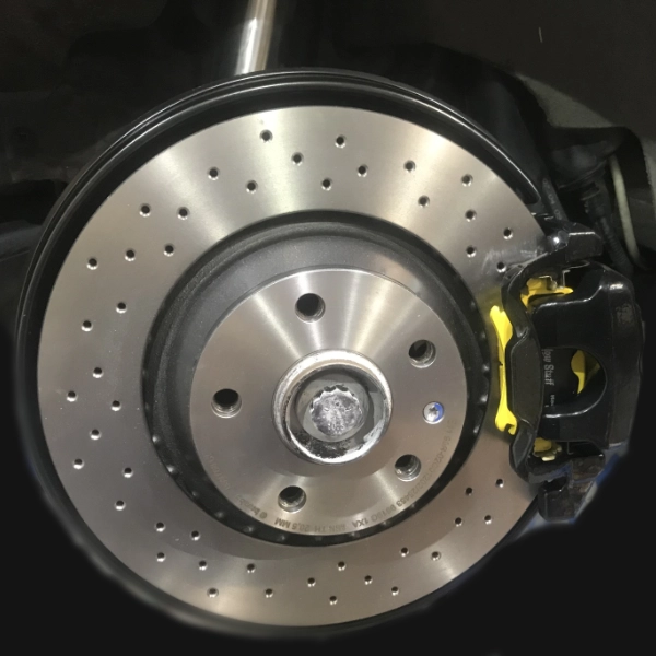 Close-up of a drilled silver car brake disc with a black and yellow brake caliper attached.