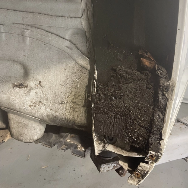 Close-up of a vehicle's wheel well area showing accumulated dirt and grime inside the metal panel.