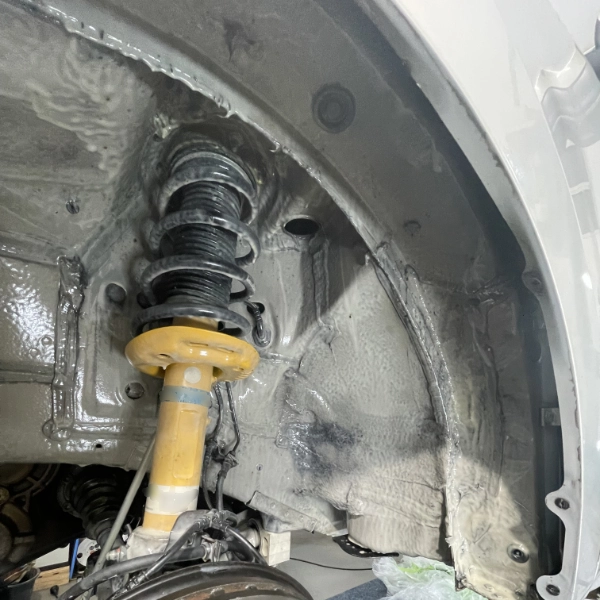 Close-up of a car's suspension system including a yellow shock absorber and coil spring inside the wheel well.