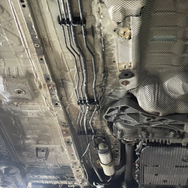 Underside of a vehicle showing metal fuel or brake lines secured to the chassis and parts of the transmission system.