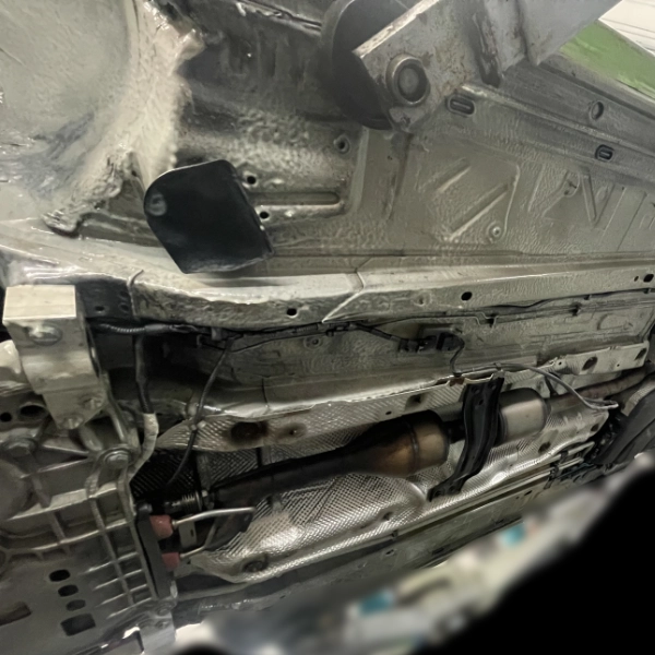 Underbody of a vehicle showing exhaust system, heat shields, and metal frame components.