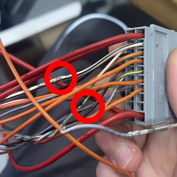 Close-up of a hand holding a gray connector with multiple colored wires, two wires circled in red showing damaged insulation.
