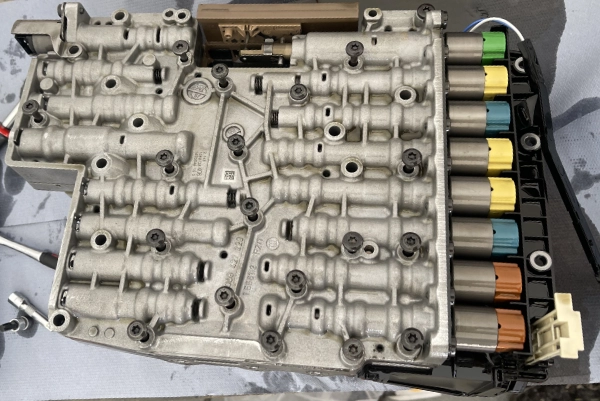 Close-up of a mechanical component with multiple valves and connectors, featuring color-coded cylindrical parts in green, yellow, blue, and brown on one side.