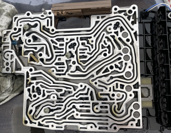 Close-up view of an automotive transmission valve body showing intricate metal channels and passages.
