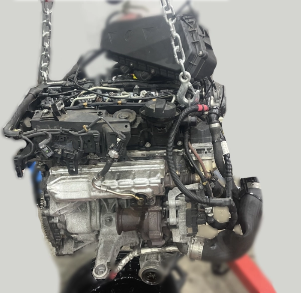 Car engine suspended by metal chains, showing various components and wiring.