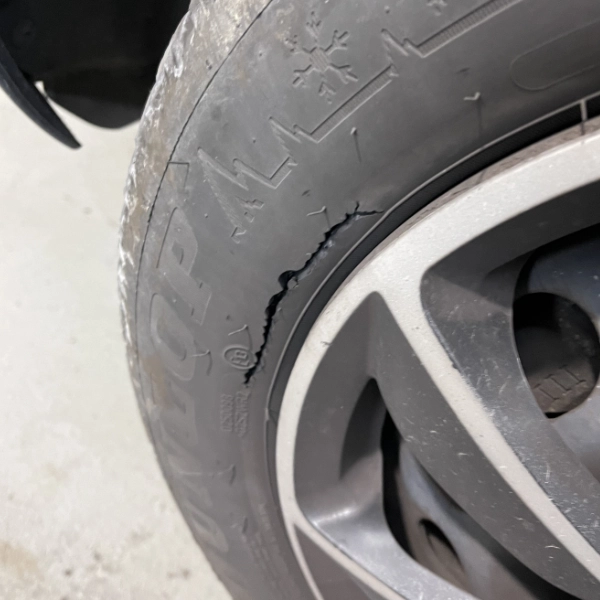 Close-up of a car tire with a large crack on the sidewall near the rim.
