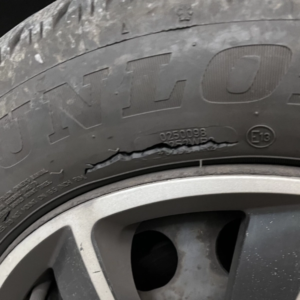 Close-up of a car tire with a large cut or tear in the sidewall near the word 'Dunlop'.