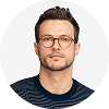 Portrait of a man with short dark hair, glasses, and a dark striped shirt against a white background.