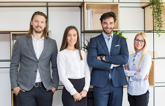 Group of four young professionals dressed in business attire standing confidently in an office setting.
