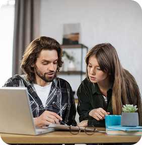 Man and woman sitting at a table, looking at a laptop screen together.