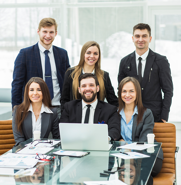 Six business professionals smiling at a conference table with a laptop and documents in a modern office.