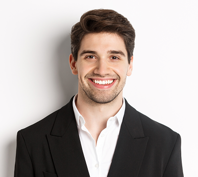 Smiling young man with short dark hair wearing a black blazer and white shirt against a white background.