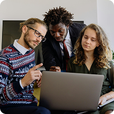 Three colleagues collaborating and looking intently at a laptop screen in an office setting.