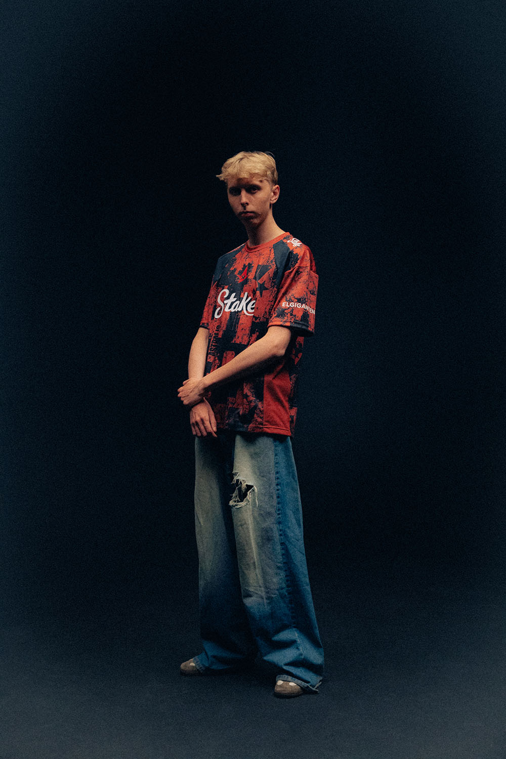 jabbi wearing an Astralis jersey and loose blue jeans, holding one wrist in front of him.
