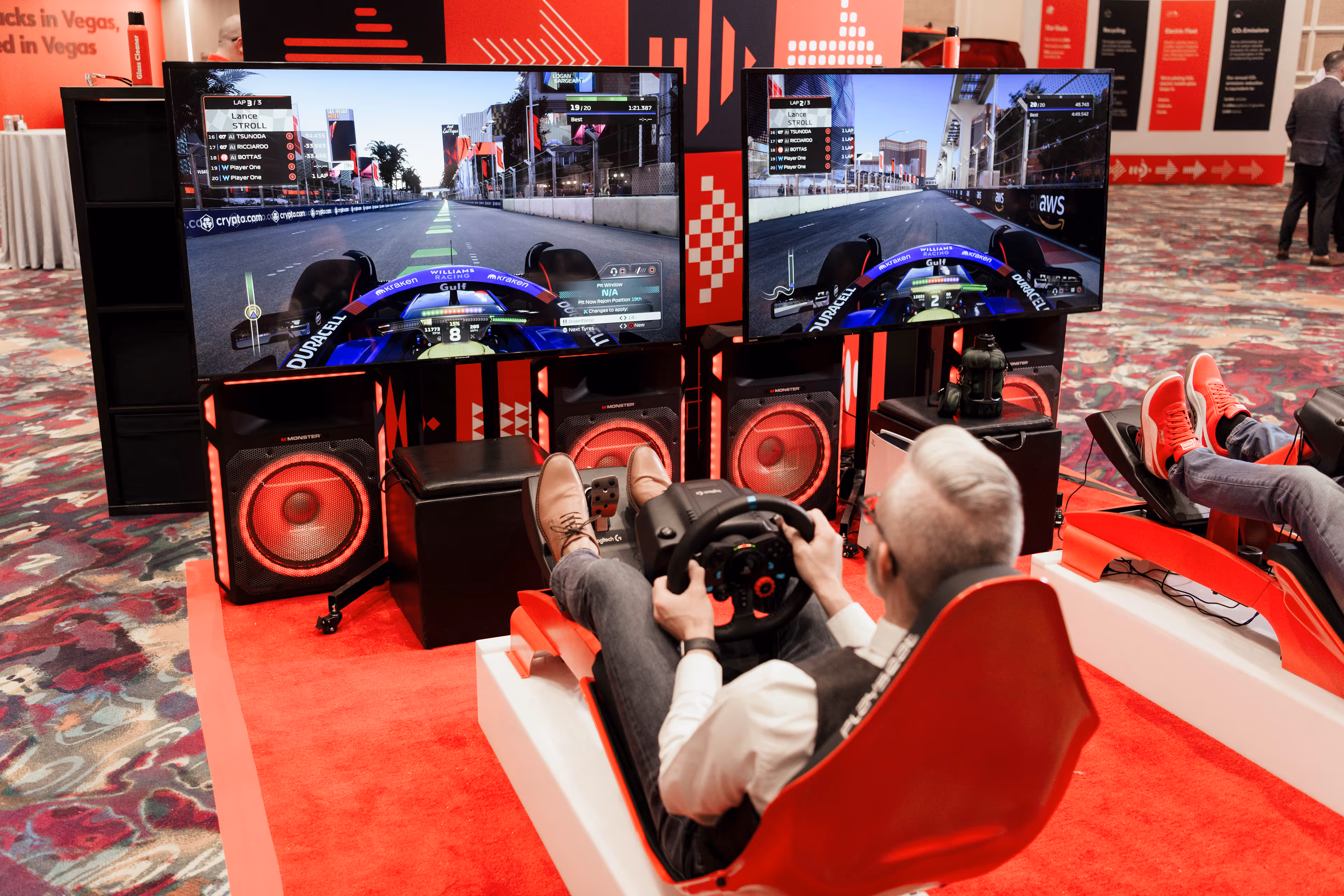Two people seated in red racing simulators playing a Formula 1 racing game on large screens.