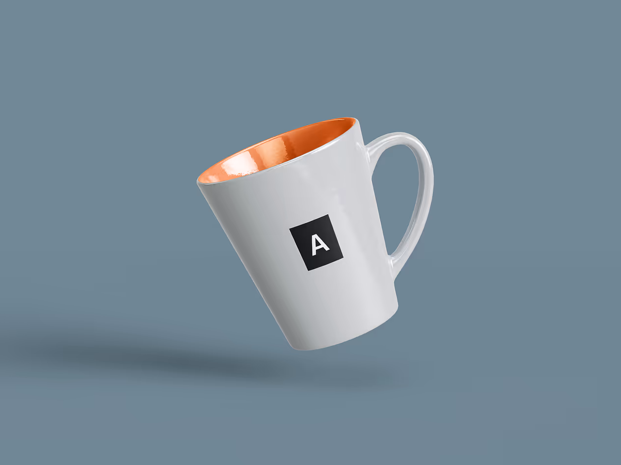White ceramic mug with an orange interior, floating against a blue background, displaying a black square logo with the letter “A.”