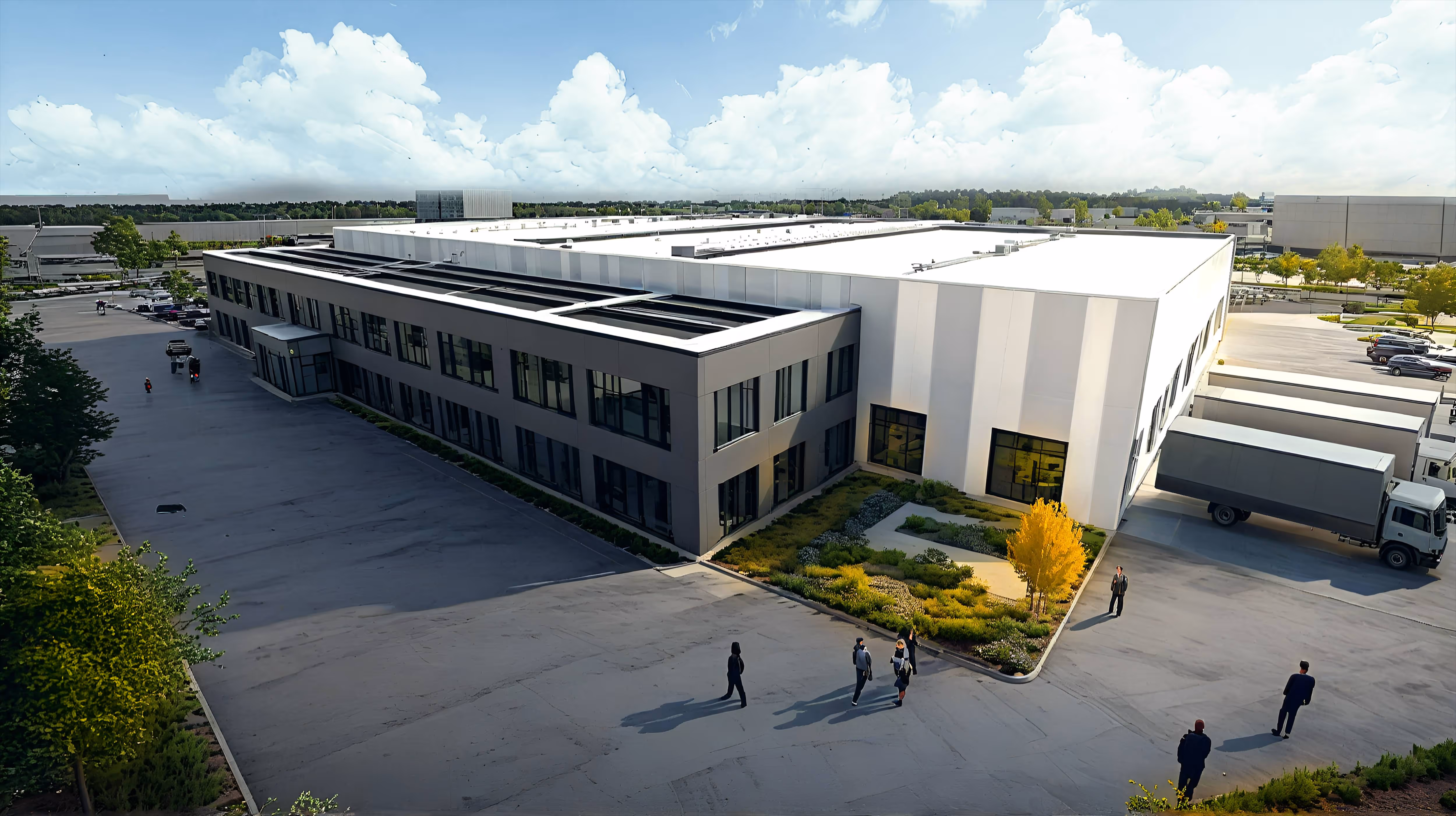 Aerial view of a modern industrial warehouse building with adjacent office space, surrounded by parking lots and several people walking nearby.