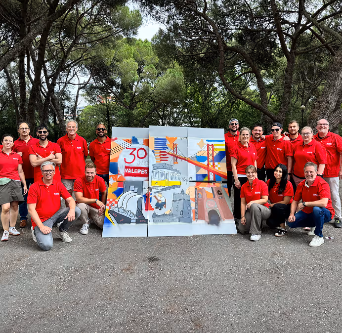 Group of people wearing red shirts posing outdoors around colorful panels depicting a bridge, tram, and cityscape.